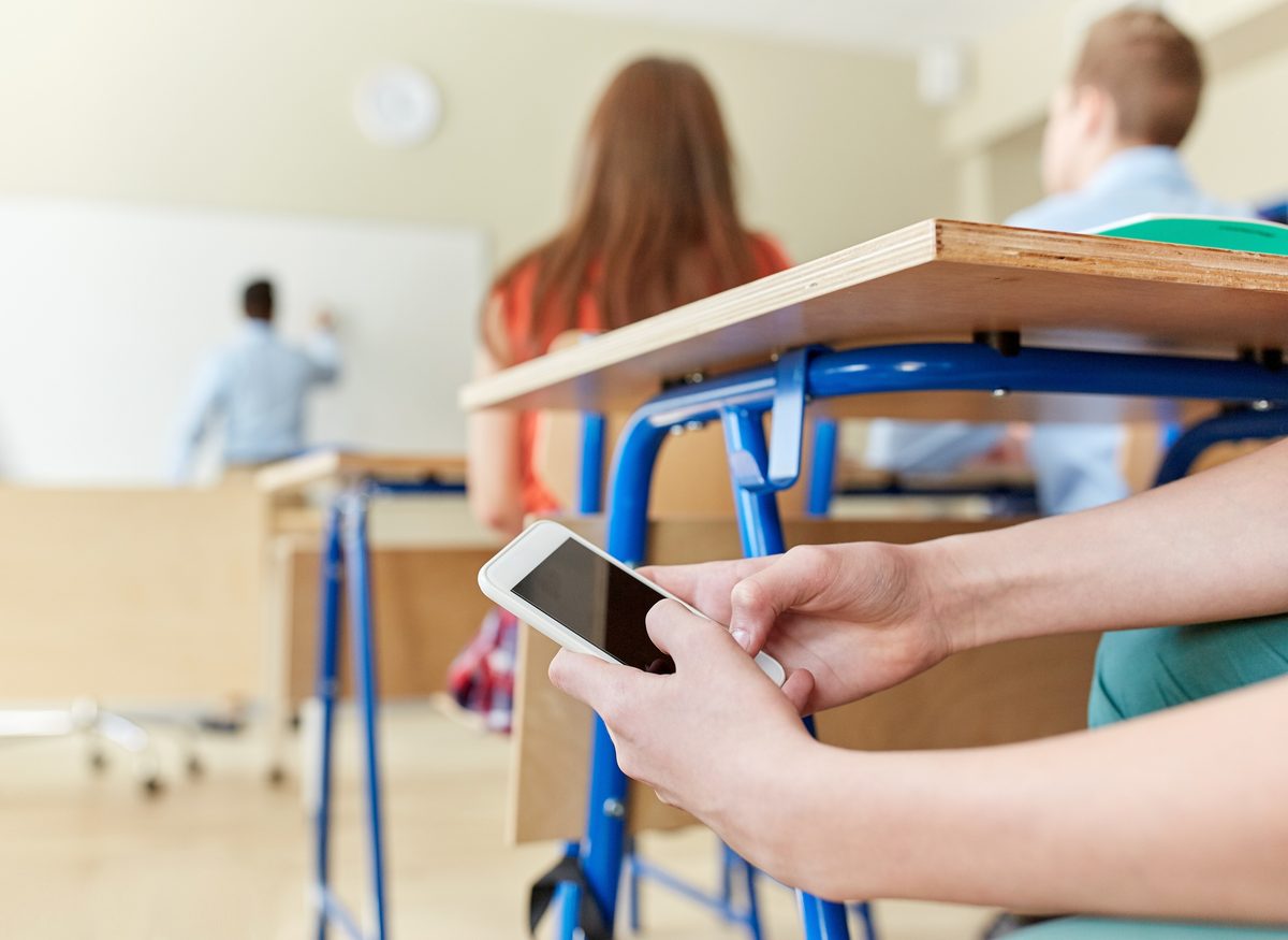 Student discreetly using a phone under a classroom desk